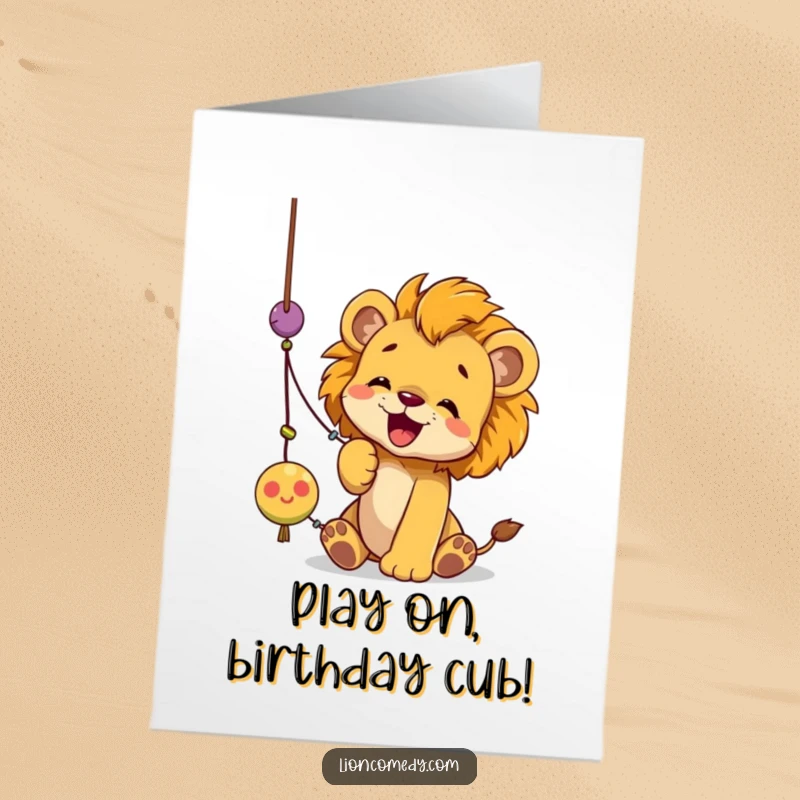Funny Free Printable Birthday Card showing a cute lion cub joyfully batting at a dangling string toy with its paw.